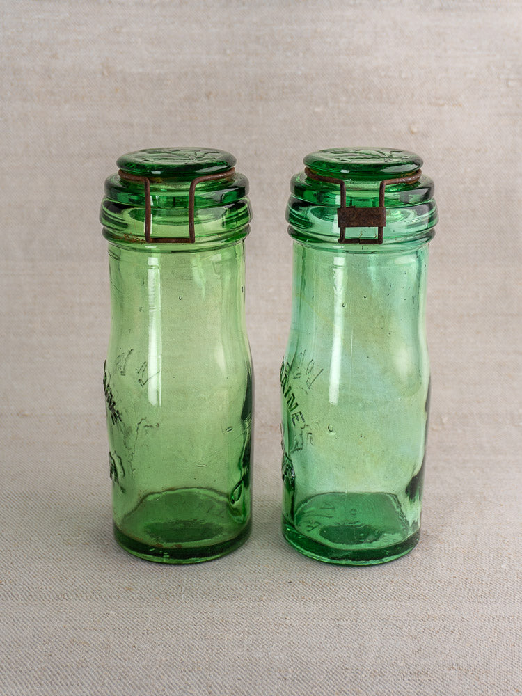 Pair of antique French La Lorraine green glass jars with thistle motif on neutral fabric background.