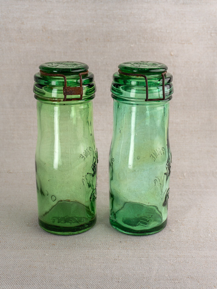 Pair of Antique French La Lorraine green glass jars with wire closures, embossed text, thistle motif, and uneven finish.