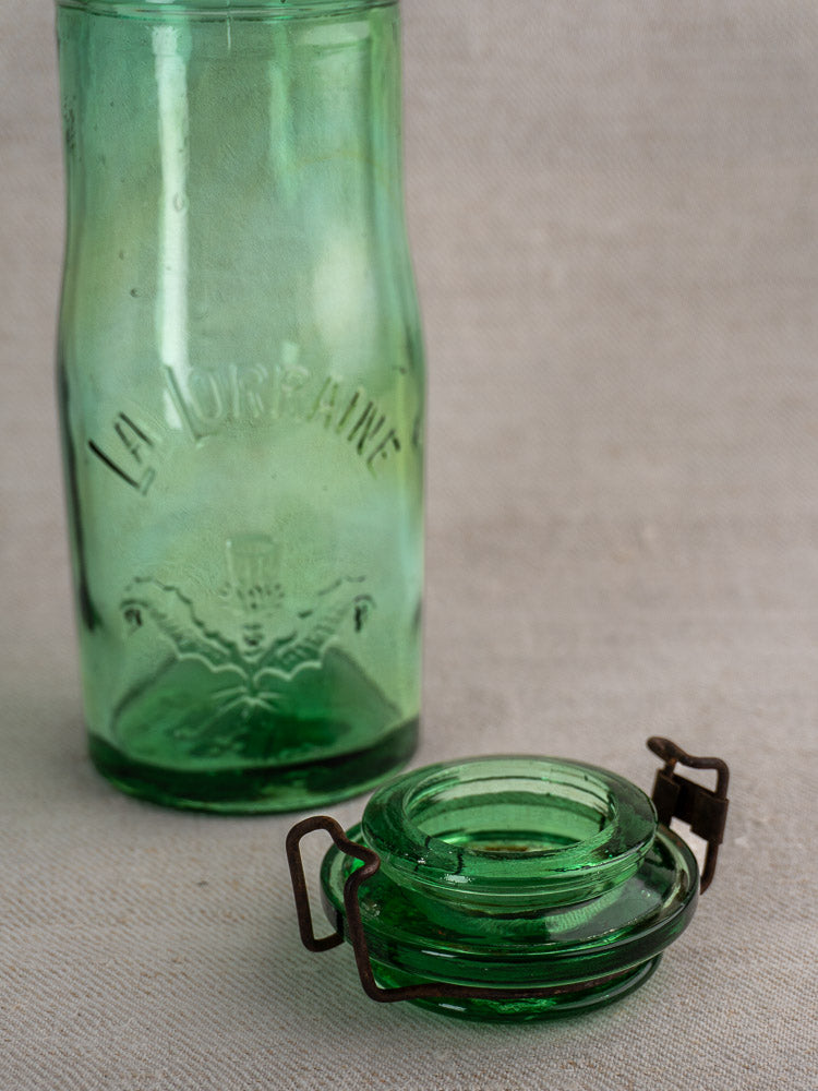 Pair of antique French La Lorraine green glass jars with thistle motifs, embossed details, and metal clasp lids.