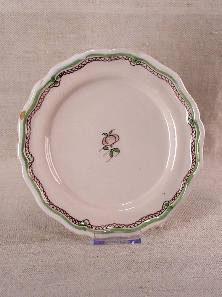 Antique French faience plate with hand-painted turnip motif, displayed upright on textured beige fabric.
