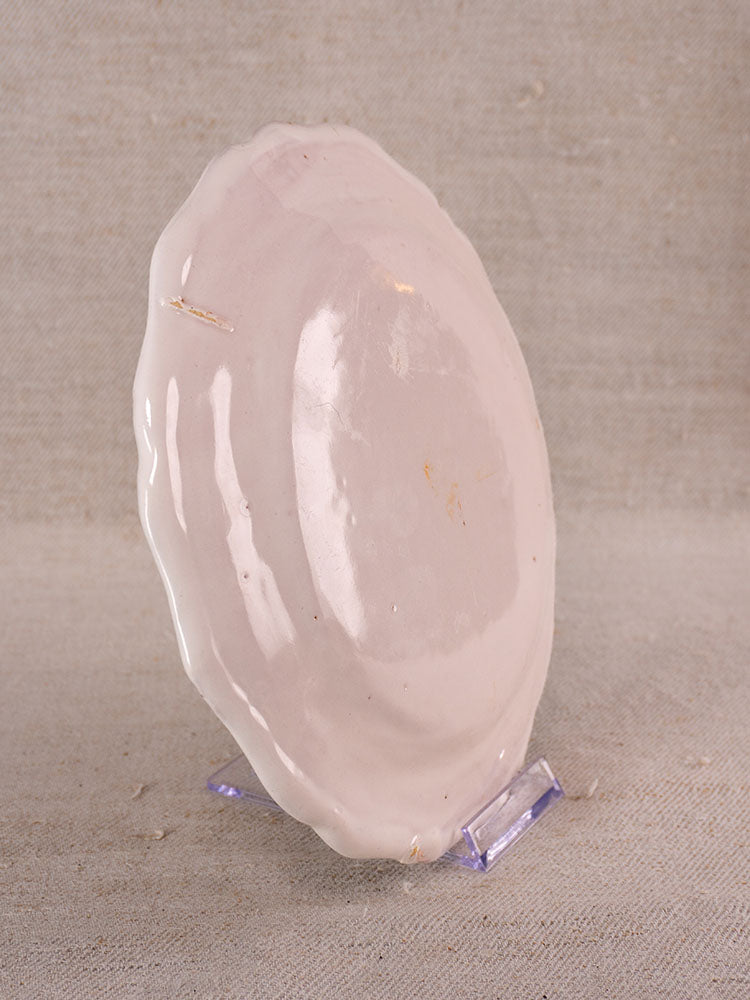 Antique French faience plate with hand-painted turnip motif, wavy oval shape, on clear stand with fabric backdrop.