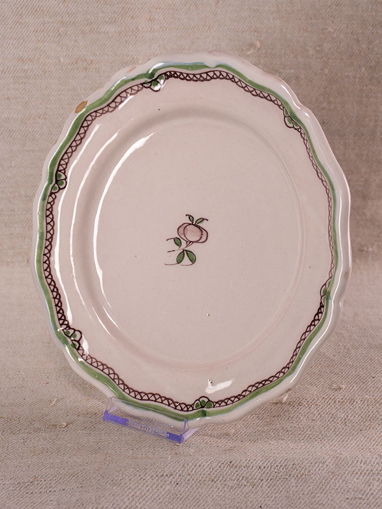 Pair of antique French faience plates with hand-painted turnip motif, scalloped edges, on clear stands against beige fabric.