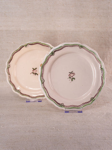 Pair of antique French faience plates with turnip motifs and scalloped edges on clear stands, neutral fabric backdrop.