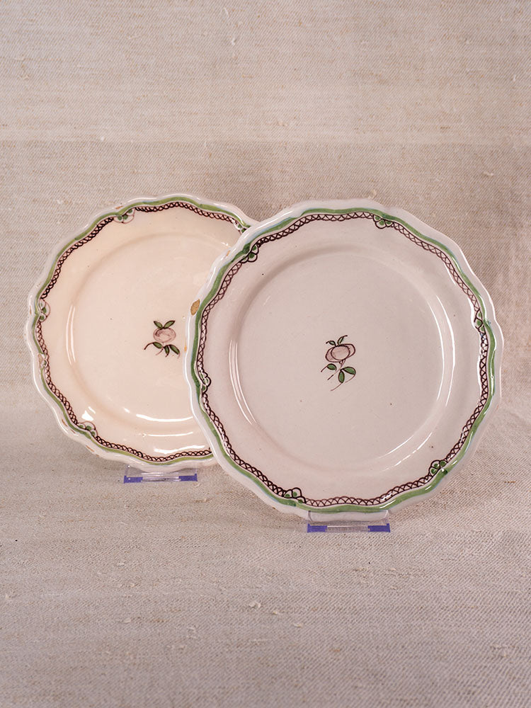 Pair of antique French faience plates with turnip motifs and scalloped edges on clear stands, neutral fabric backdrop.