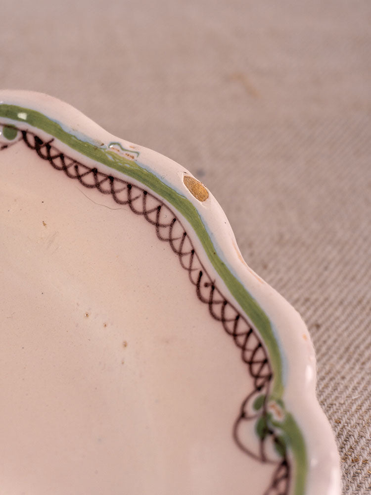 Antique French faience plate with scalloped edge, hand-painted turnip motif, small chip, on beige textured fabric. Sold as a pair.
