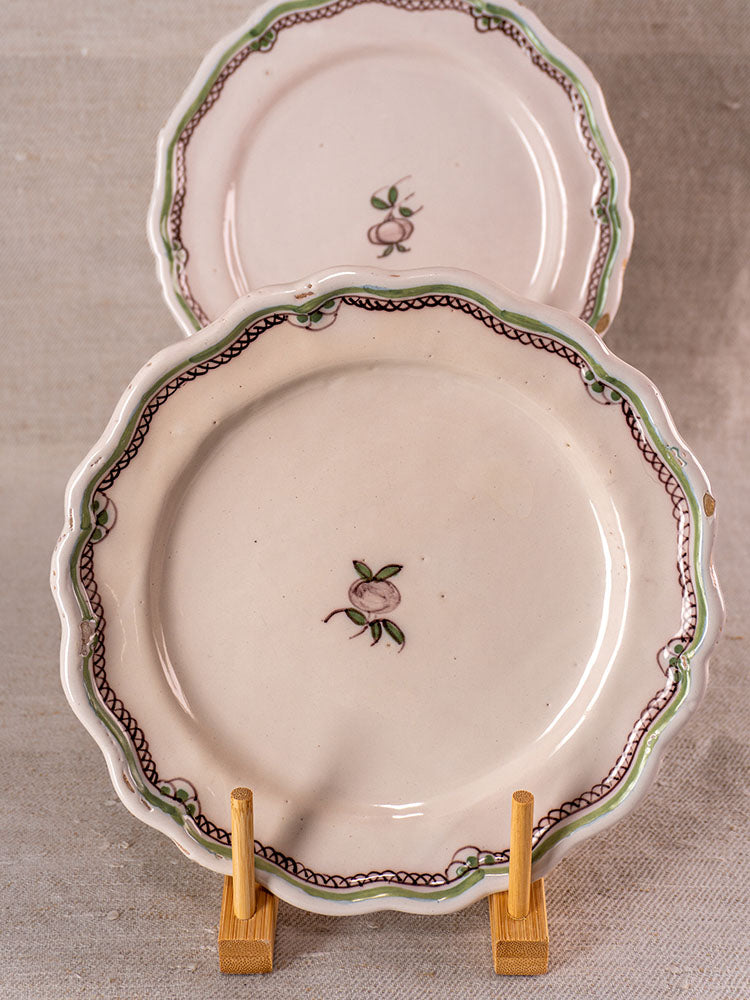 Antique French faience plates with hand-painted turnip motifs and scalloped edges on wooden stands, neutral fabric backdrop.