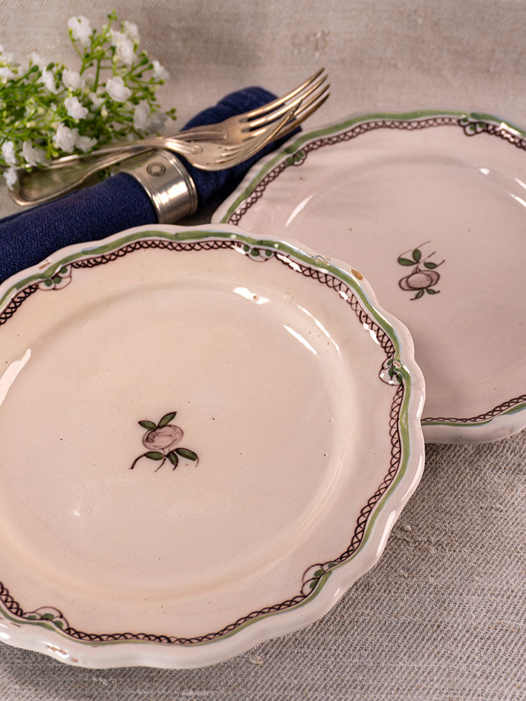 Pair of antique French faience plates with turnip motifs and scalloped edges on clear stands, neutral fabric backdrop.