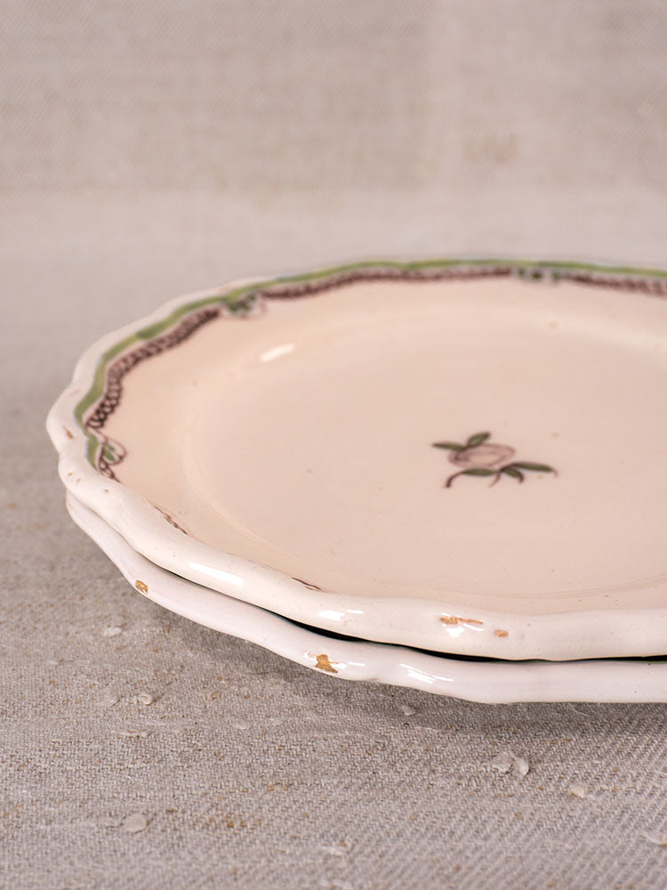 Antique French faience plates with hand-painted turnip motif, scalloped edges, minor chips, on textured beige fabric.