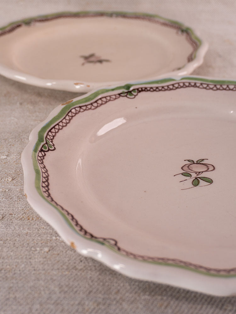 Antique French faience plates with scalloped edges, hand-painted turnip motifs, on textured beige fabric.
