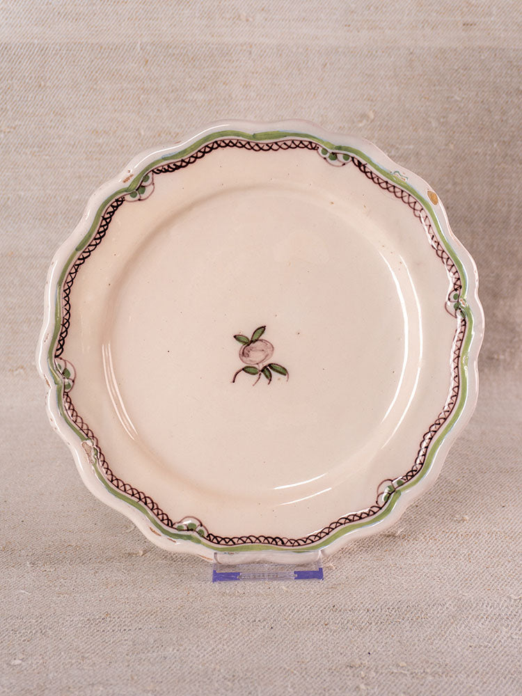 Antique French faience plate with cream glaze, scalloped edges, turnip motif, and wavy green-brown border on display stand.