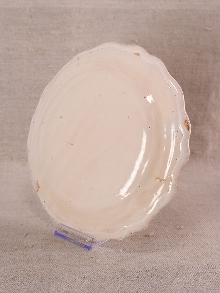 Antique French faience plate from Eastern France with hand-painted turnip motif, displayed on a clear stand against fabric.