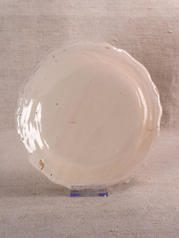 Antique French faience plate with hand-painted turnip motif, shown upright on clear stand against neutral fabric background.