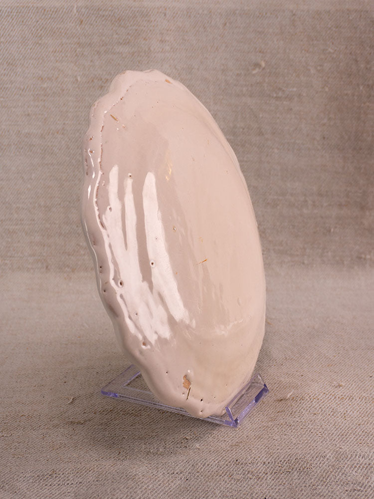 Antique French faience plate with hand-painted turnip motif on clear stand, set against beige textured fabric.