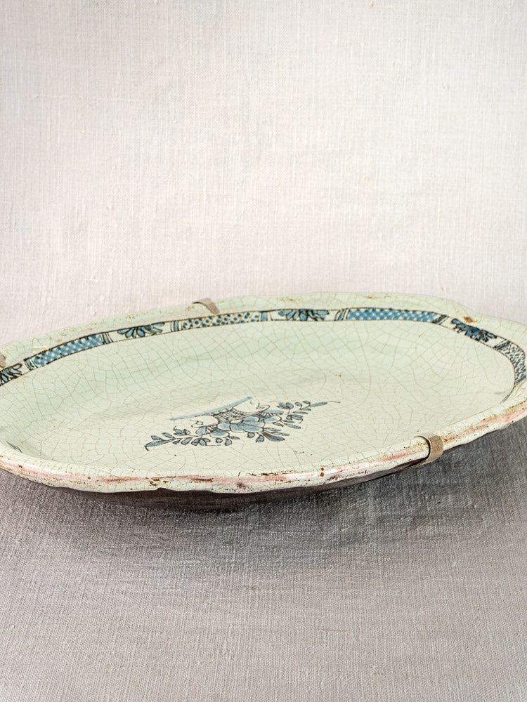 Pair of antique French Rouen-style faience platters with crackled glaze, blue edges, and floral centers on light textured surface.