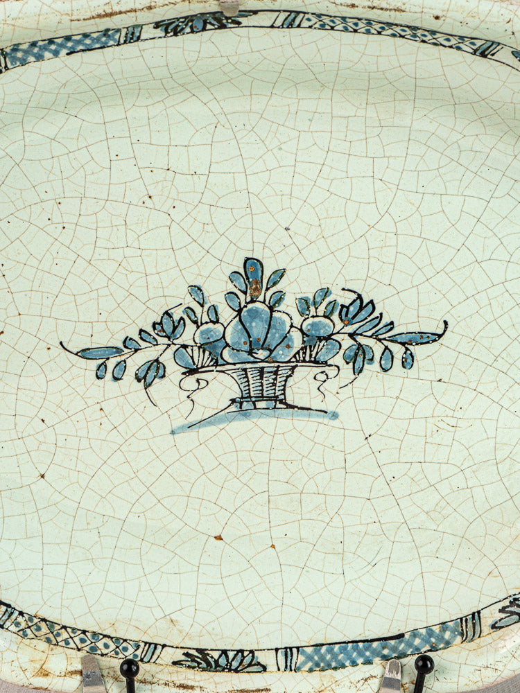 Antique French faience platter with crackled glaze, blue floral basket motif, and patterned rim border.