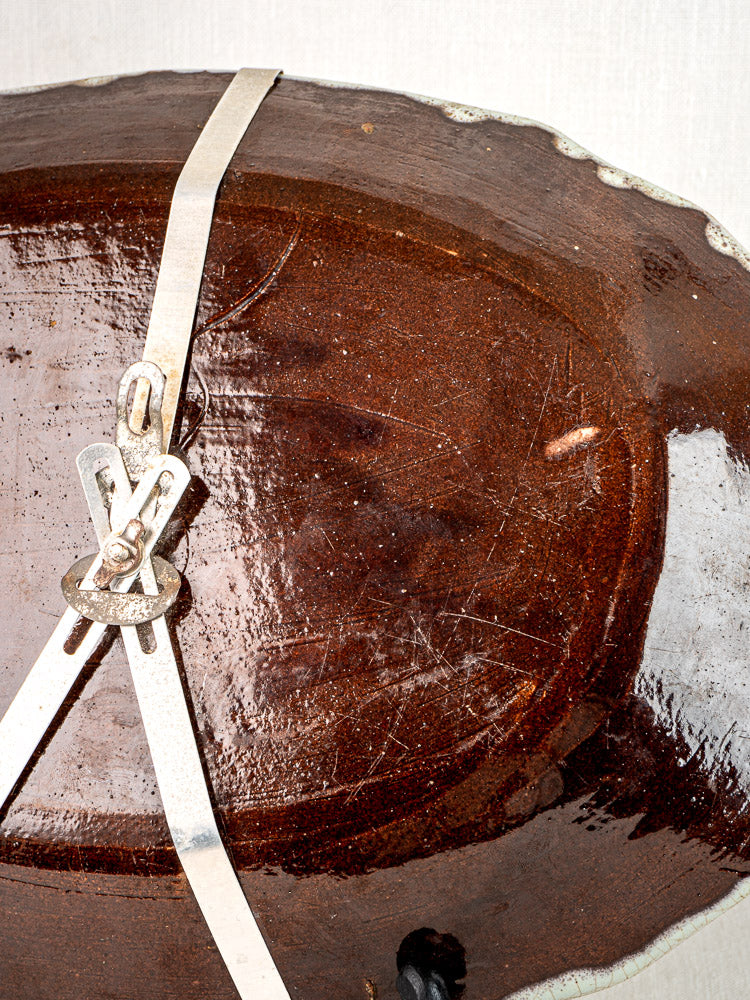 Underside of antique French Cul Noir faience platter with scratches and attached hanging wires, on light background.