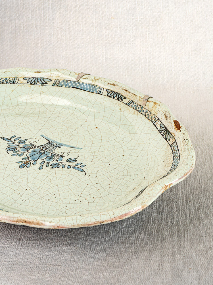 Antique French faience plate with faded blue floral motif and worn edges on textured surface.