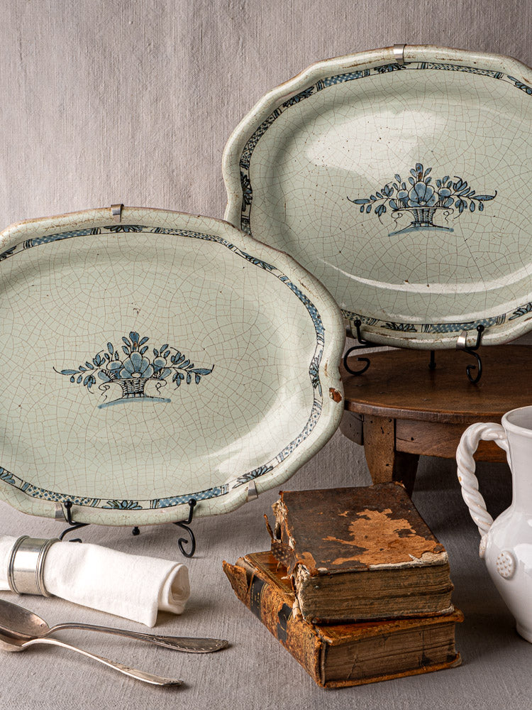 Pair of antique French Cul Noir faience platters with blue floral designs on rustic wood surface.