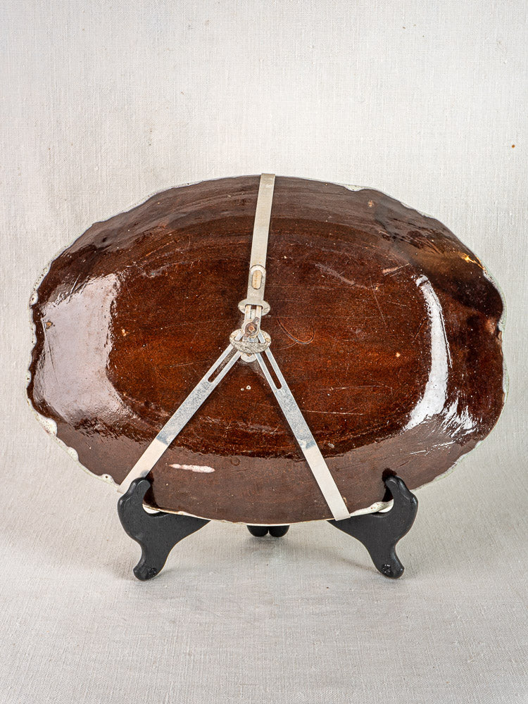 Large oval brown glazed ceramic platter, c. 1750–1780, on black stand with metal braces, neutral fabric backdrop.
