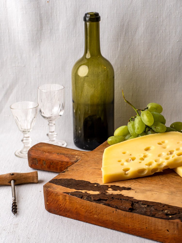Antique 19th c. French live edge cutting board with wine bottle, glasses, grapes, cheese, and corkscrew.