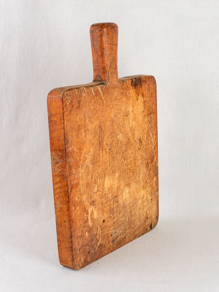 Antique 19th-century French live edge cutting board with a thick handle and worn, scratched surface.