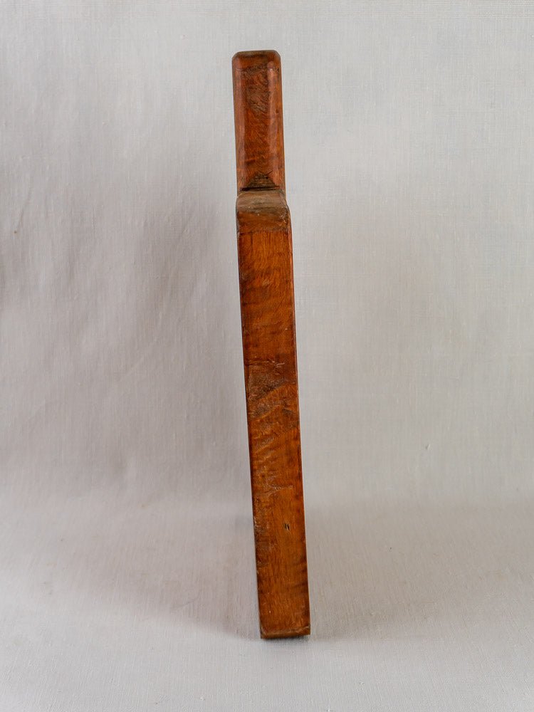 Antique 19th-century French live edge cutting board upright on a light plain background, narrow side visible.