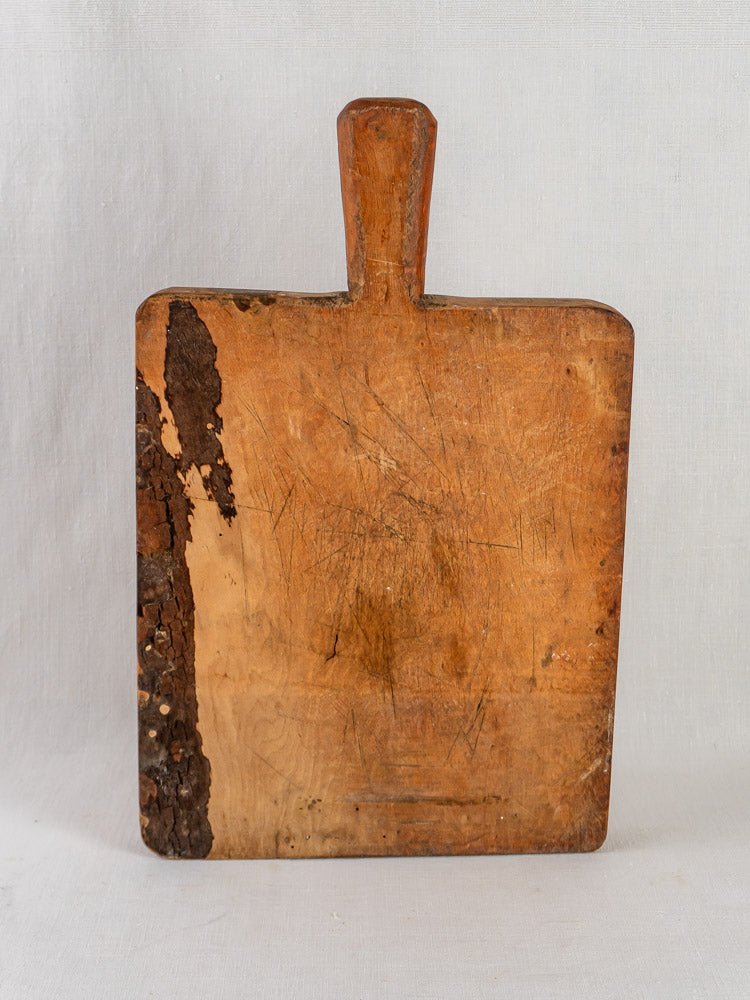 Antique 19th-century French live edge cutting board with handle and natural bark accent.