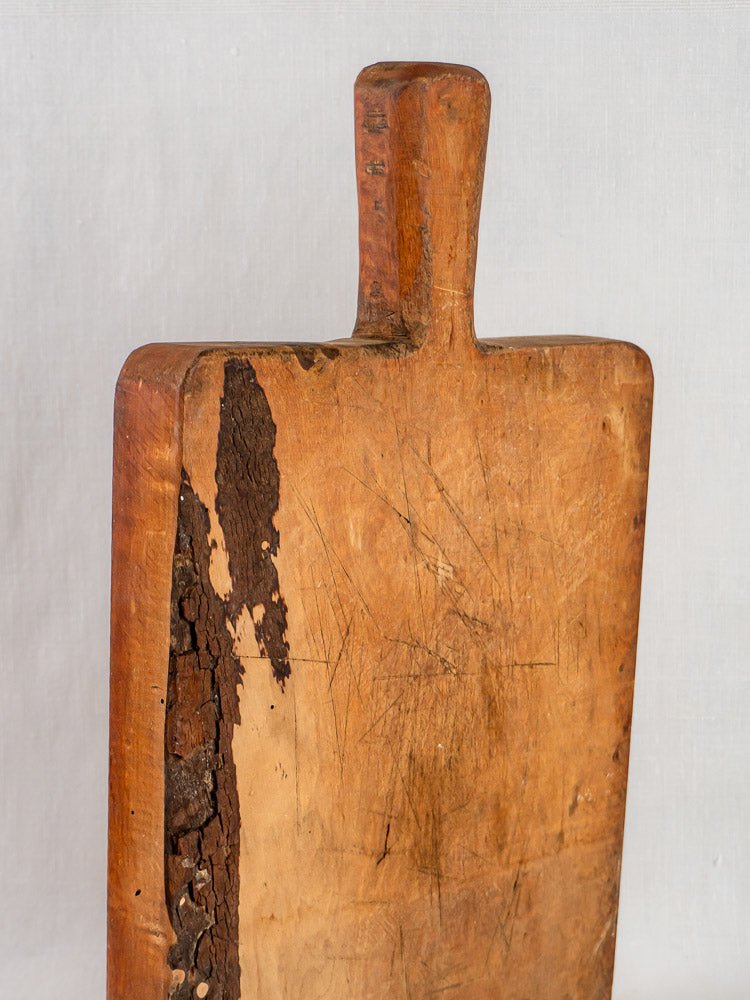 Antique 19th c. French live edge cutting board with handle, distressed surface, plain background.