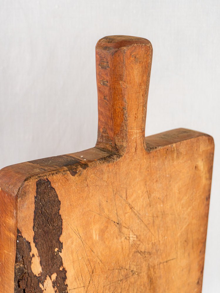 French antique live edge cutting board with handle, deep knife marks, and aged wood patina.