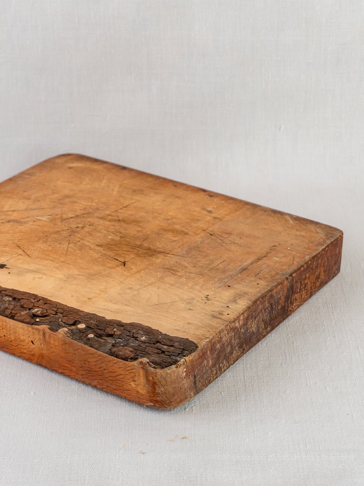 Antique 19th-century French live edge cutting board with bark edge, shown on light gray fabric.