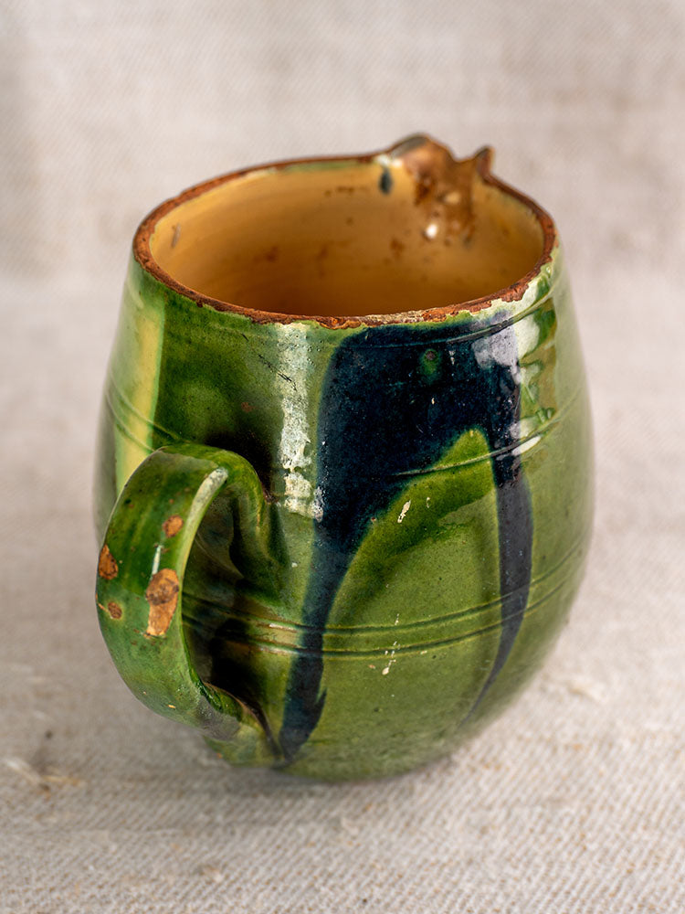 Antique French Jaspe pottery pitcher from Savoie with green floral glaze on textured neutral fabric background.