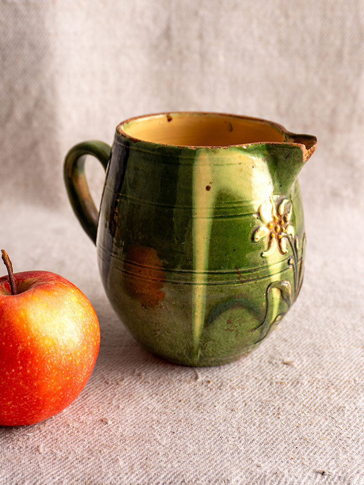 Antique French Jaspe Pottery Pitcher from Savoie with green floral glaze, next to a red apple on beige textured fabric.