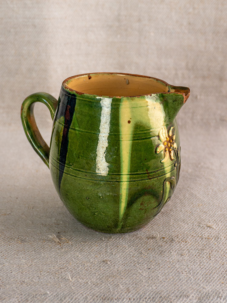 Antique French Jaspe pottery pitcher from Savoie with green glaze and floral motifs on textured beige fabric.