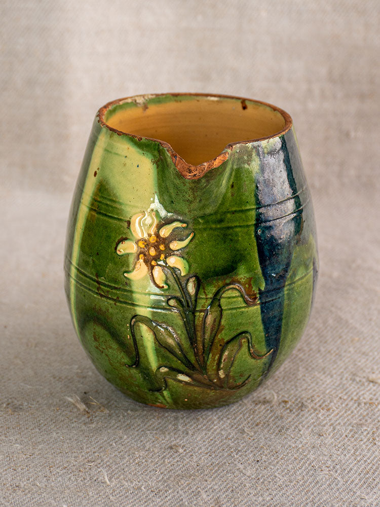 Antique French Jaspe pottery pitcher in Savoie earthenware, green and blue glaze, yellow and white florals, chipped rim, beige fabric background.