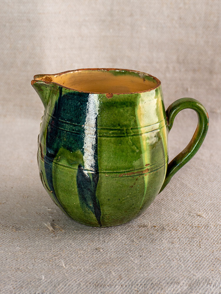 Antique French jaspe pottery pitcher from Savoie with green floral glaze on red earthenware, displayed on beige textured fabric.