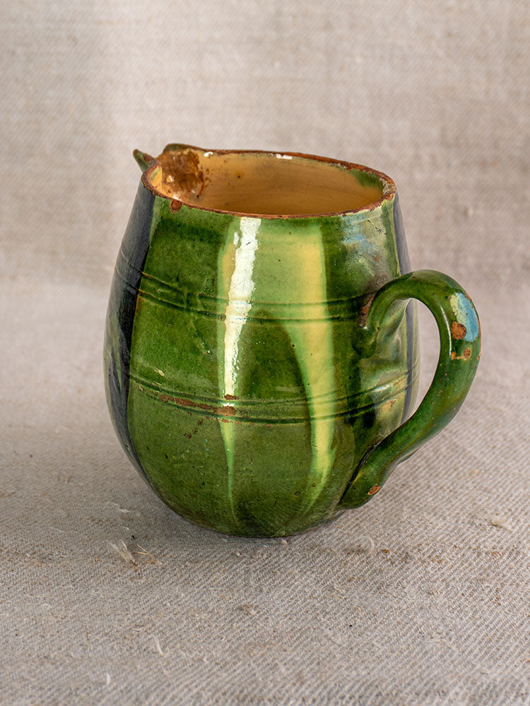 Antique French Jaspe Savoie earthenware pitcher with green glaze, floral motif, handle, spout, and minor chips on fabric.