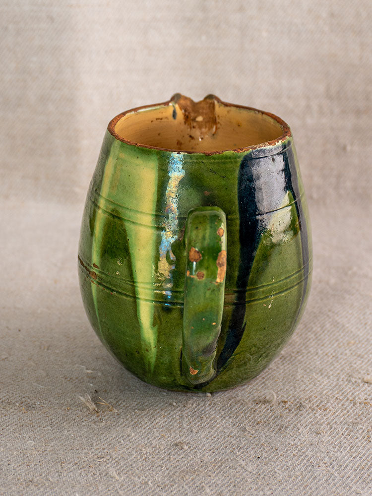 Antique French jaspe pottery pitcher with green glaze and floral motif on a textured beige cloth.