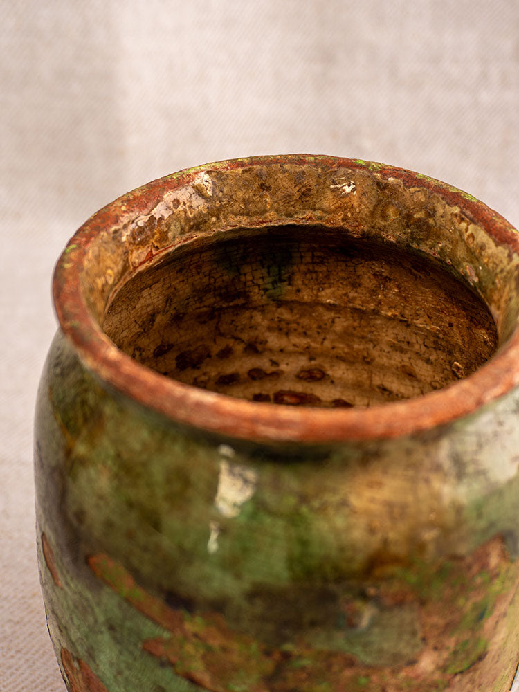 Antique French confit pot with textured green and brown glaze, 19th century, on neutral fabric background.
