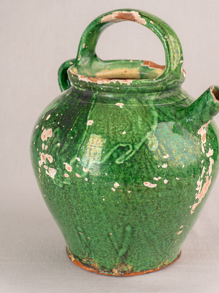 Antique French green glazed earthenware gargoulette jug with side spout and large handle, worn glaze, neutral background.