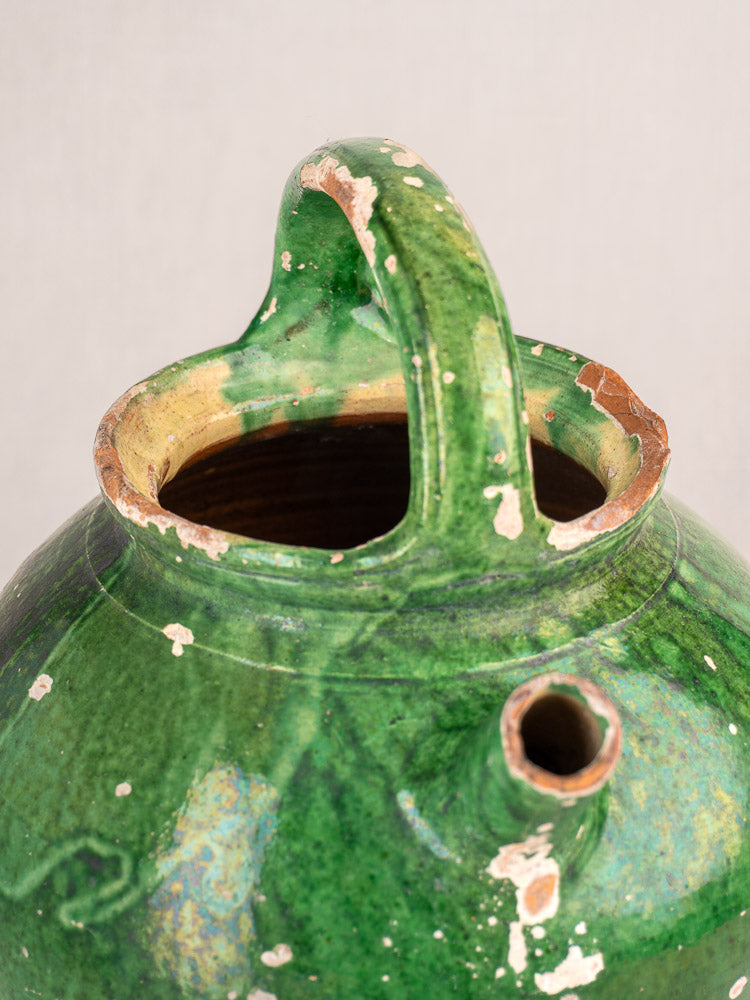 Antique French Provençal green glazed earthenware gargoulette jug with large handle and exposed brown clay chips.