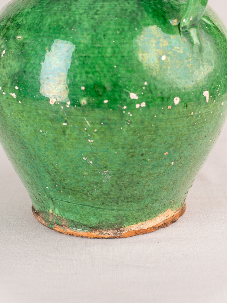 Antique French gargoulette with chipped green glaze and worn base, Provençal earthenware on light fabric.