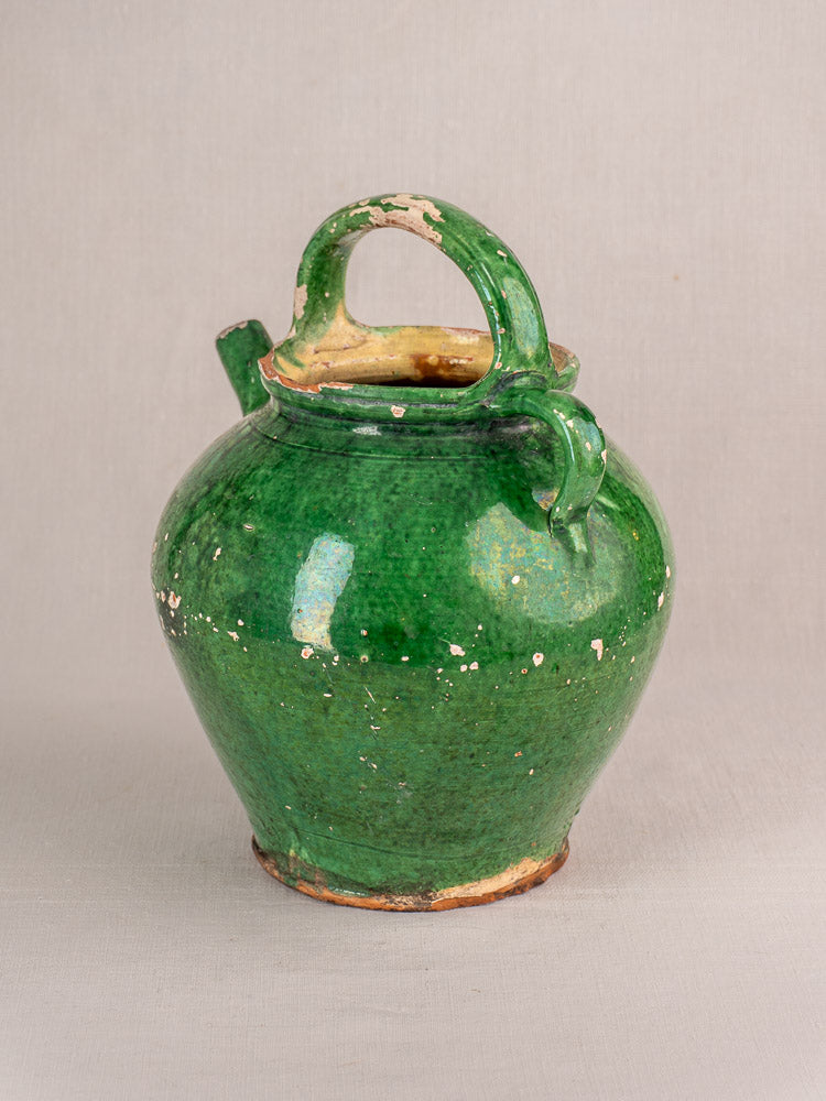 Antique French green-glazed earthenware gargoulette jug with spout, handle, and visible clay chips on neutral background.