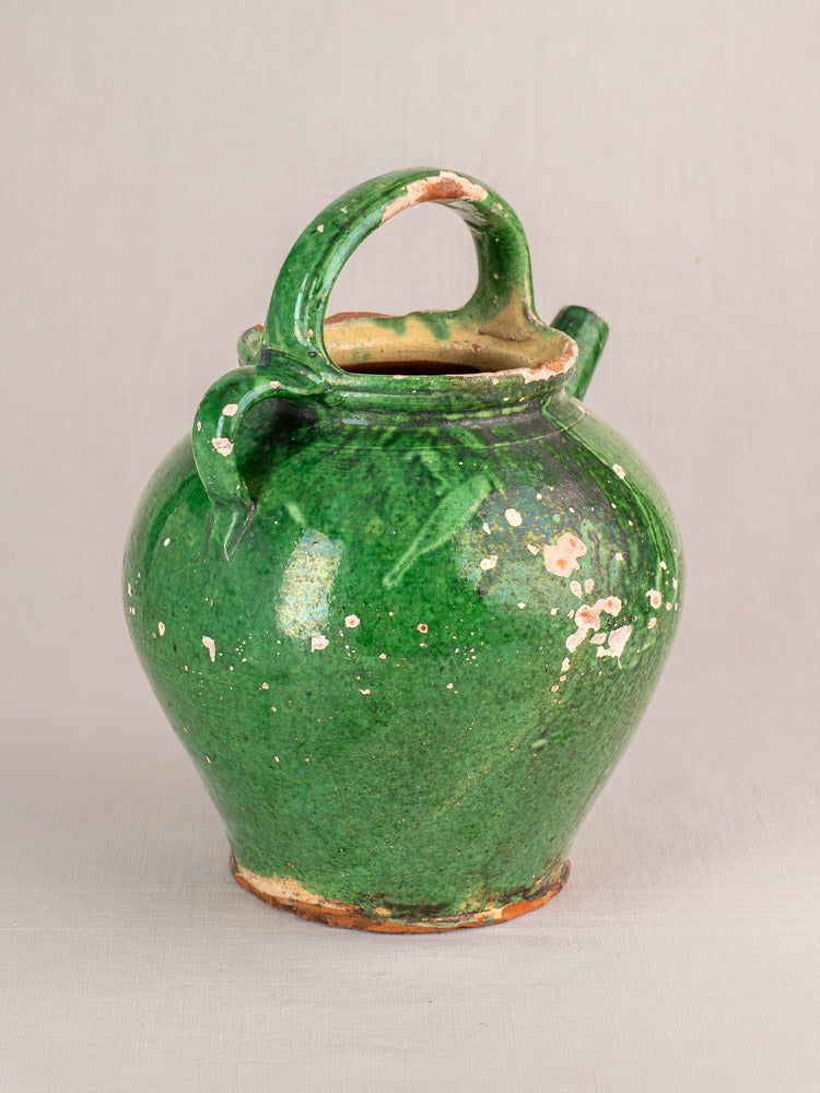 Antique French green-glazed earthenware gargoulette with rounded body, top handle, worn patches, on a plain surface.