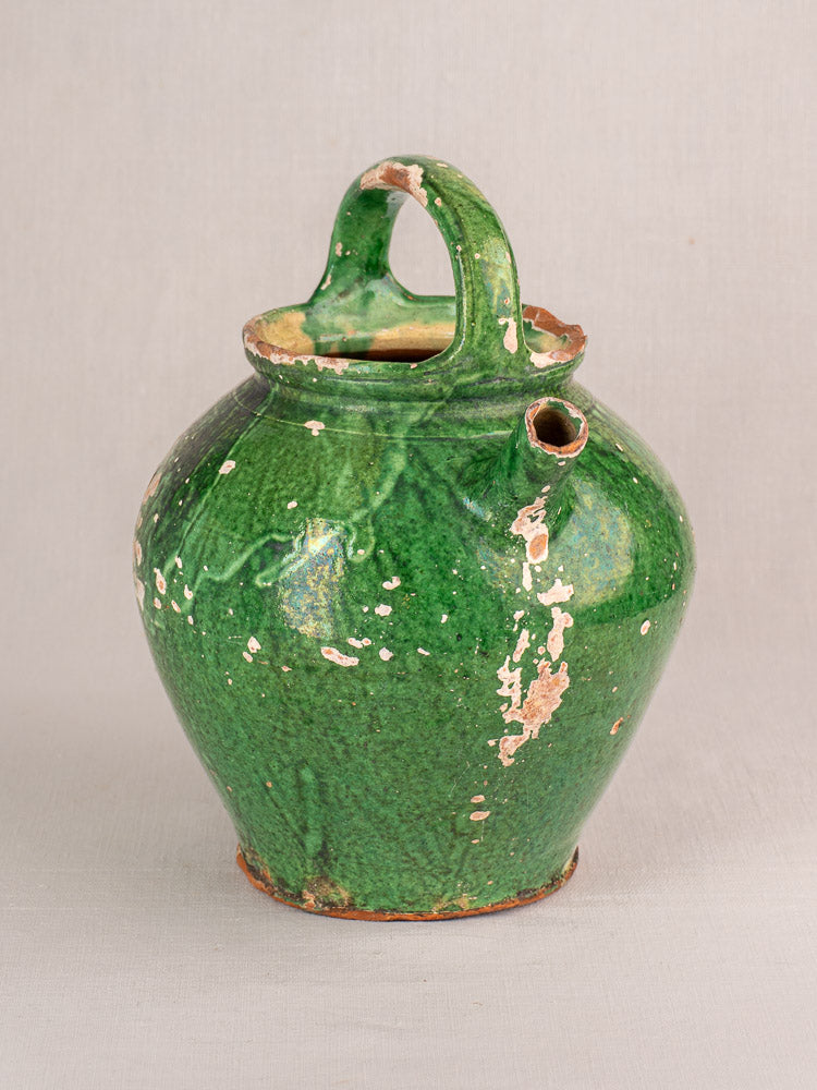 Antique French green-glazed earthenware gargoulette jug with rounded body, side spout, and visible clay beneath chipped glaze.