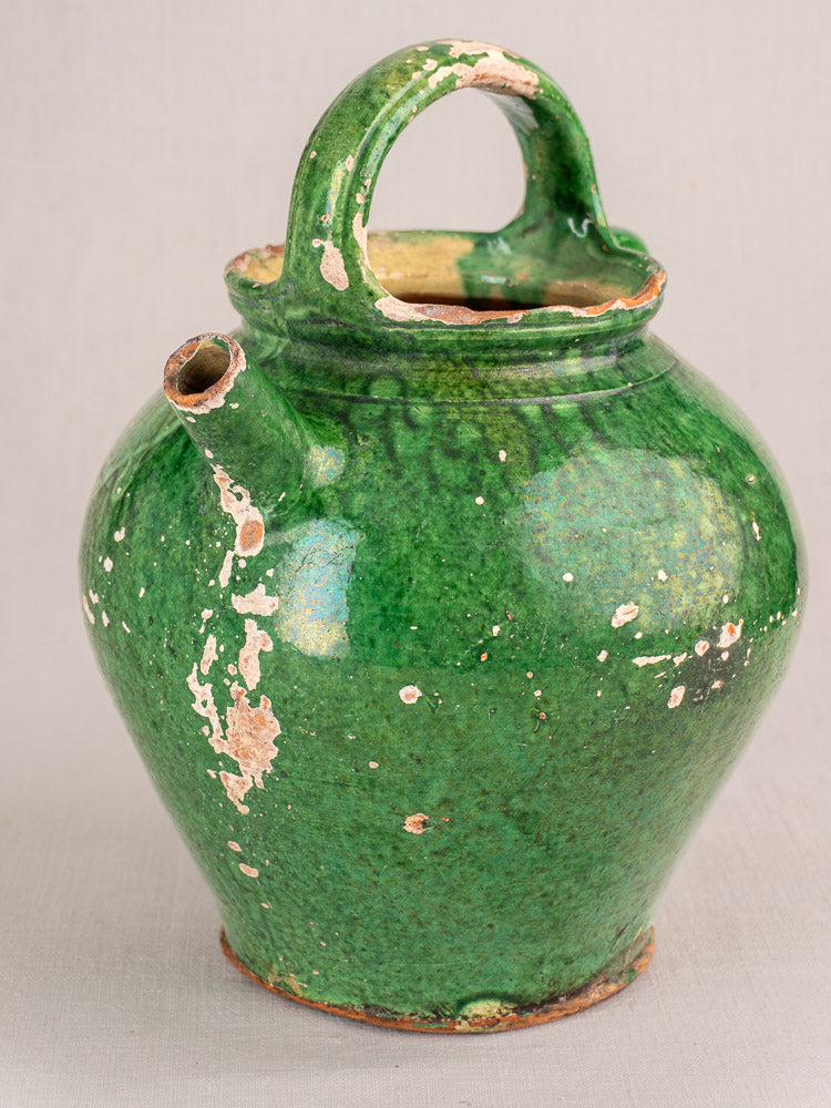 Antique French green-glazed earthenware gargoulette jug with handle and side spout, worn base, on neutral background.