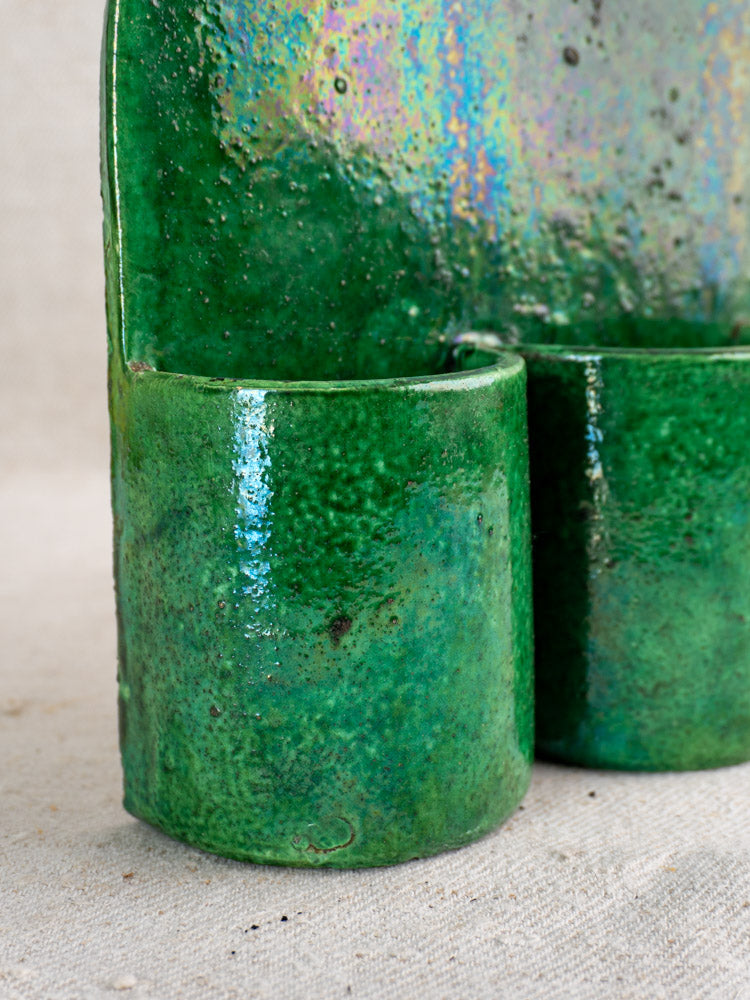 Antique French green glazed earthenware wall utensil holder with cylindrical and curved forms, terre vernissée finish, fabric backdrop.
