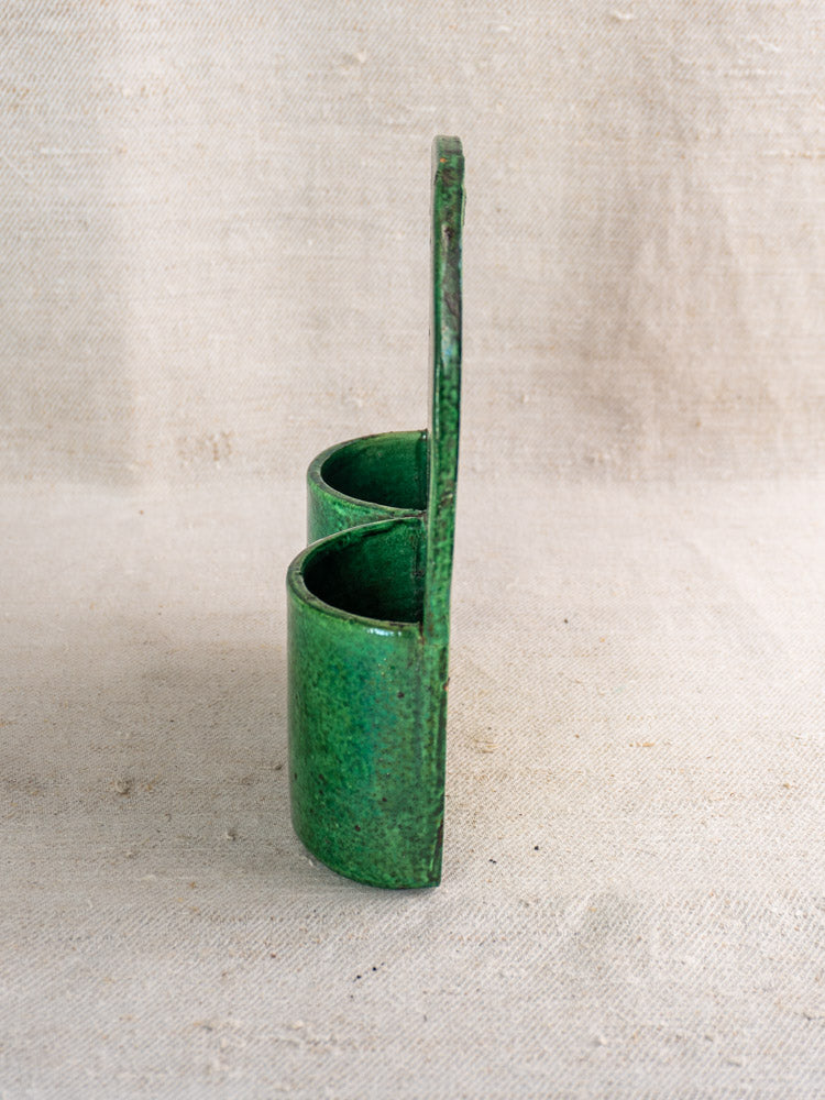 Antique French green glazed earthenware wall utensil holder with twin cylinders, late 19th-early 20th century, on beige fabric.
