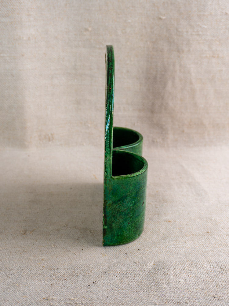 Antique French green glazed earthenware wall utensil holder, two cylindrical pockets, side view on beige fabric background.