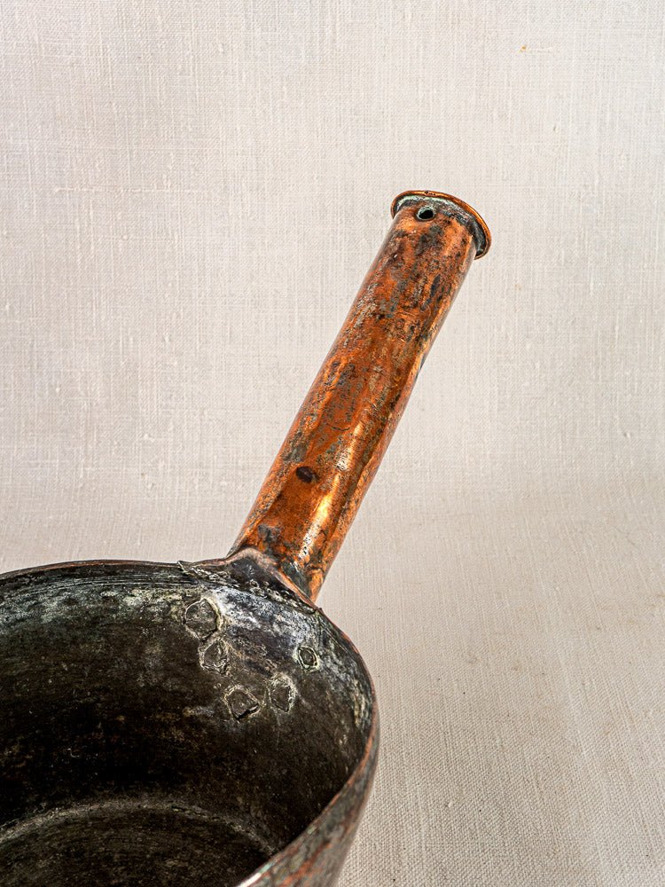 French hand-forged copper saucepan detail with timeworn, hammered surface and elongated handle on fabric.