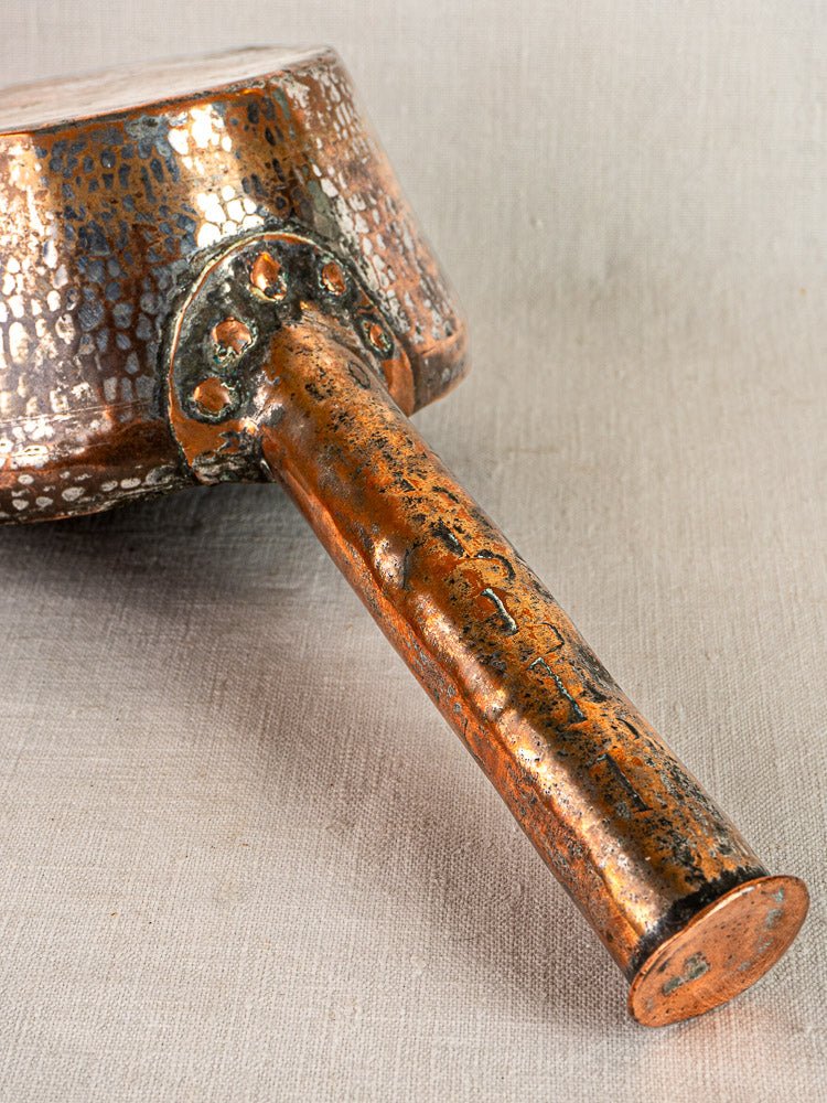 Hand-hammered French copper saucepan with textured surface and aged handle on beige fabric.